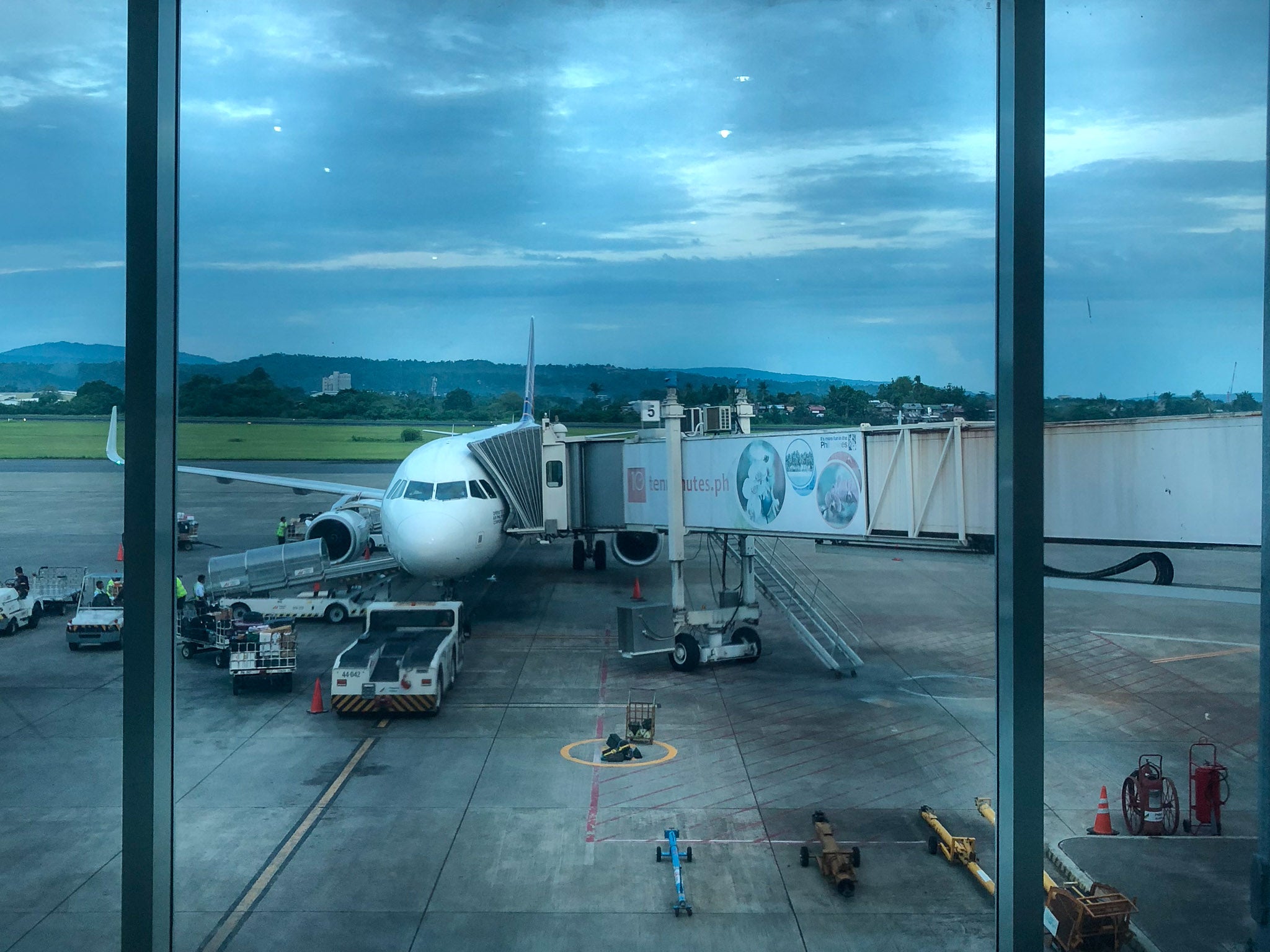 Aircraft at a gate at Francisco Bangoy International Airport in Davao at dusk, hills behind the runway