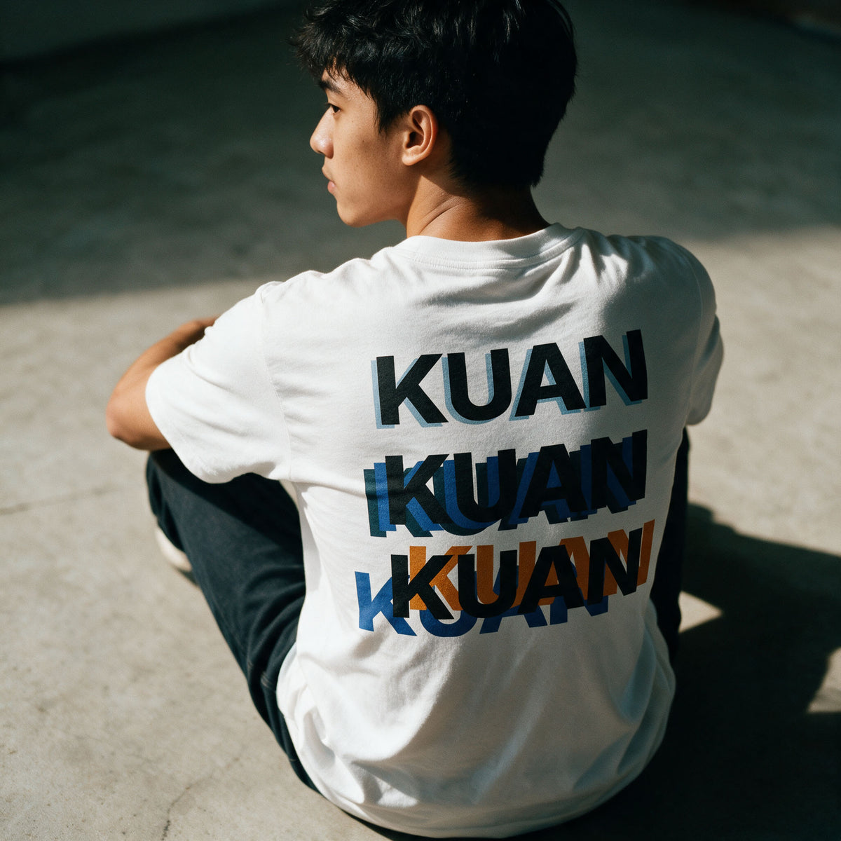 Detail of the Kuan tee back print on white cotton, three overlapping KUANs in black, blue and orange