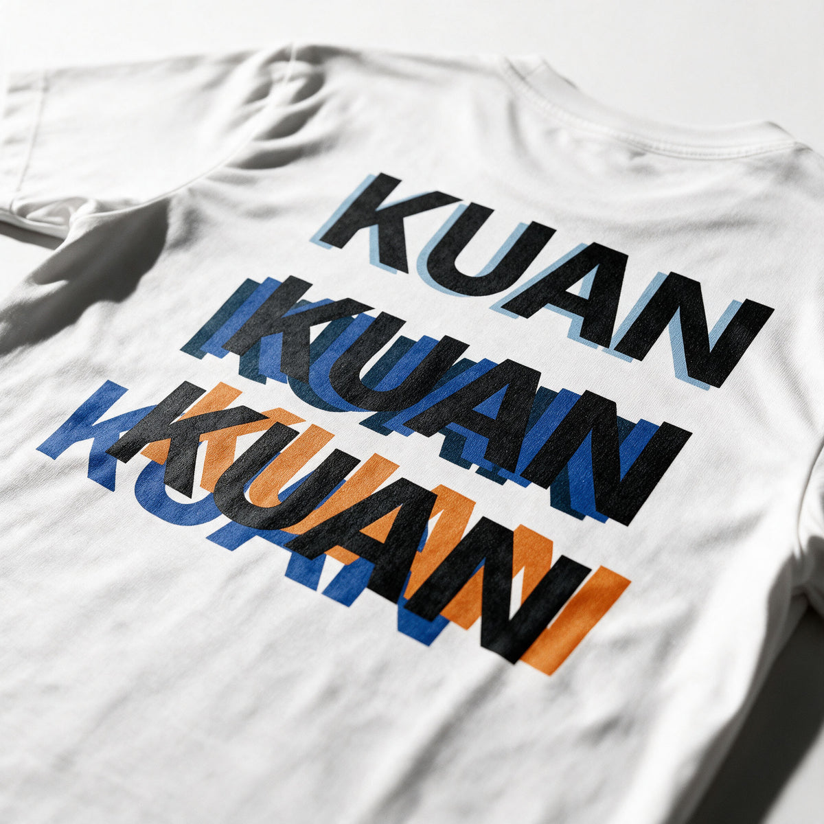 Close-up of the Kuan tee back print in white, the word stacked three times out of register in black, blue and orange