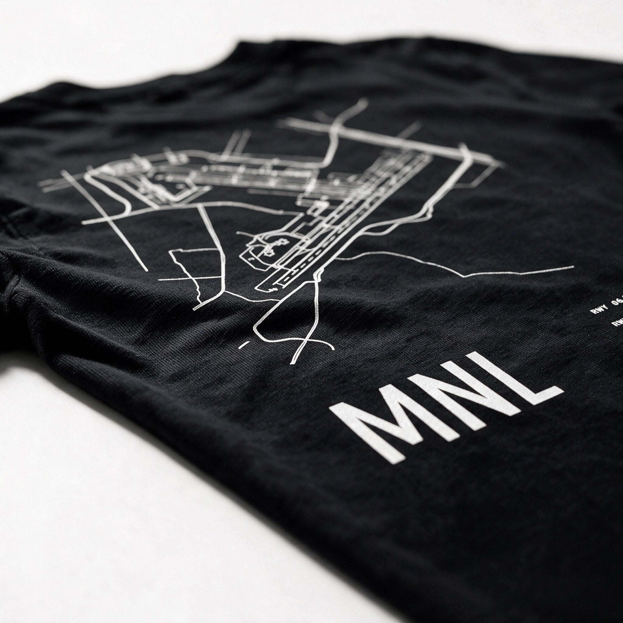 Airport Series MNL tee folded on white, close on the printed Ninoy Aquino runway map and the MNL code