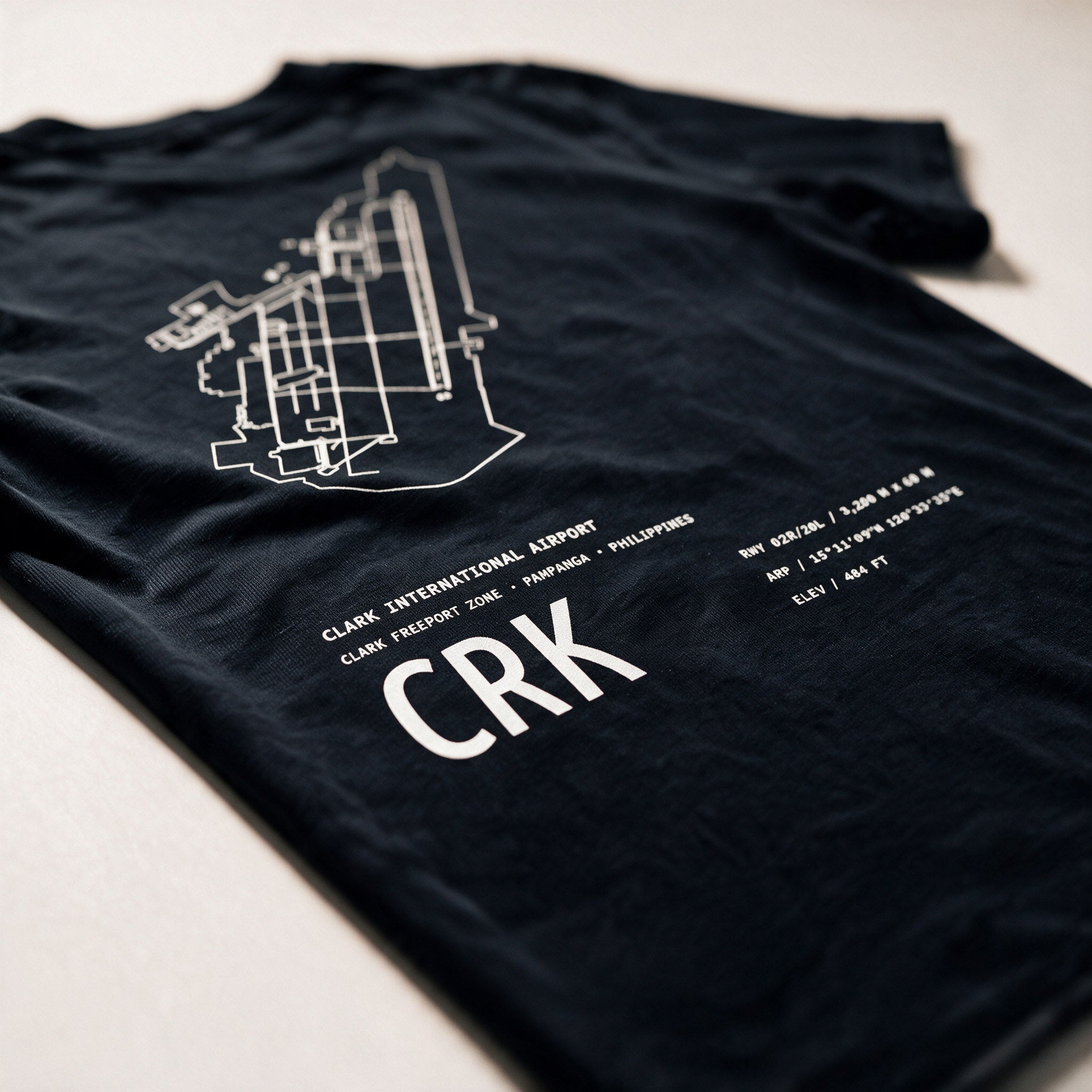 Airport Series CRK tee folded on a pale surface, the white Clark airport chart and CRK code across the back