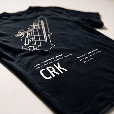Airport Series CRK tee folded on a pale surface, the white Clark airport chart and CRK code across the back