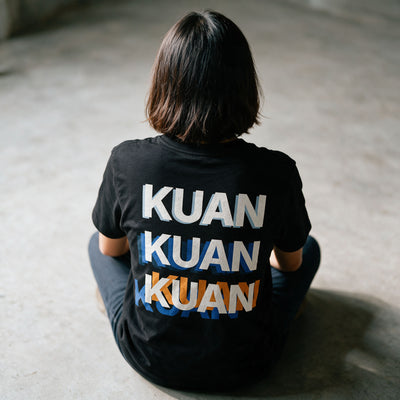 Close-up of the Kuan tee back print in Midnight Black, the word stacked three times out of register in white, blue and orange