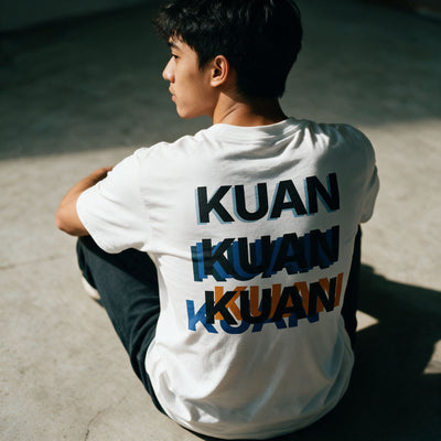Detail of the Kuan tee back print on white cotton, three overlapping KUANs in black, blue and orange