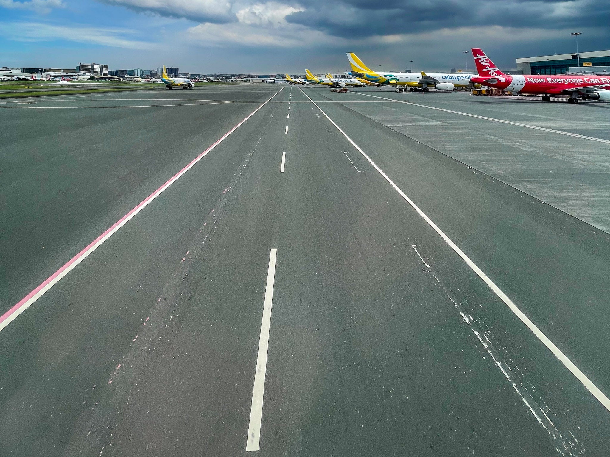 Taxiway at Ninoy Aquino International Airport under storm cloud, aircraft at the terminal beyond