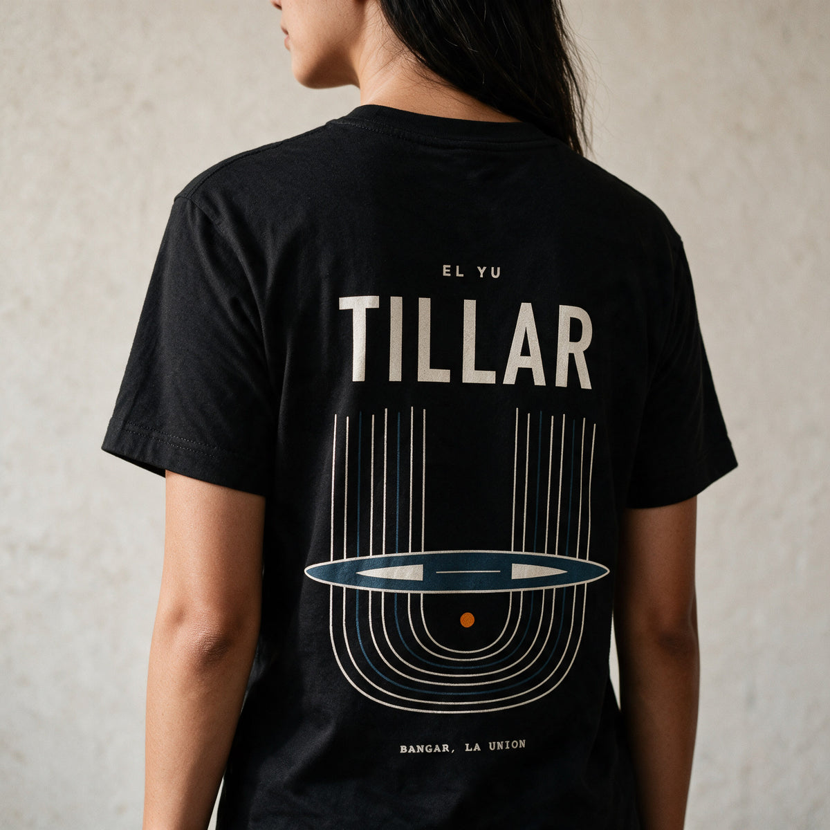 Woman in the Midnight Black Tillar tee, back view, TILLAR over the handloom print in cream and blue